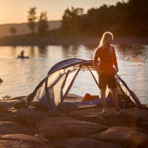 women in front of a tent on a cliff with a kayak in the background